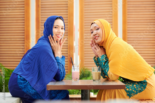 Beautiful yoing muslim women in traditional dresses resting at outdoor cafe with delicious sweet cocktails photo