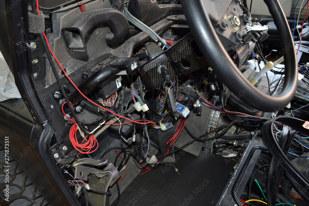 A lot of ravel multicolored wires from the car wiring lies in the cabin of dismantled car with connectors and plugs, a view through the window inside the battered car. Auto service industry