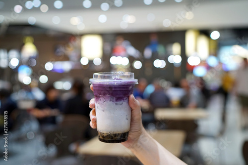 Purple sweet potato milk tea - Hand holding a glass of iced taro latte with boba or golden bubble on blurred background, Most Popular in Taiwan.