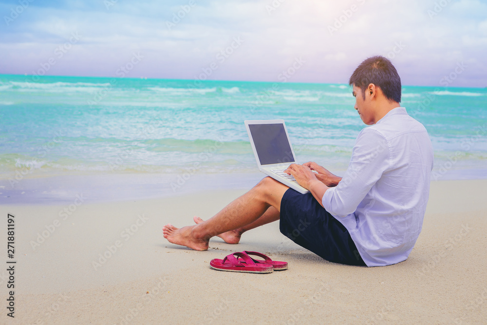 Young man working with laptop computer during tropical beach vacation. Outdoor office concept
