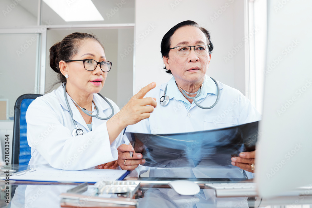 Fototapeta premium Serious concerned Vietnamese doctors holding lungs x-ray and reading results of its interpretation on computer screen