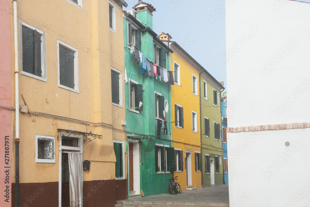 Colorful houses on the Italian island Burano, province of Venice, Italy. Multicolored buildings in fog, Italian courtyard with dry laundry outdoor.