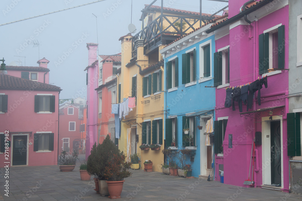 Colorful houses on the Italian island Burano, province of Venice, Italy. Multicolored buildings in fog, Italian courtyard with dry laundry outdoor.