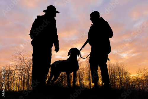 Silhouette of a hunter with a gun in the reeds against the sun, an ambush for ducks with dogs 