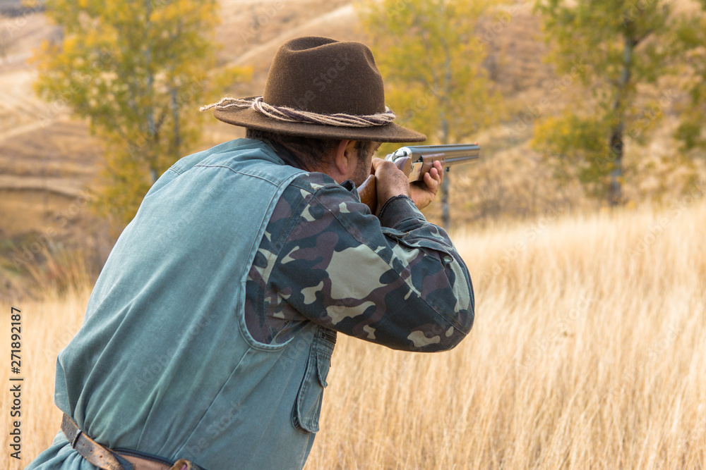 Fototapeta premium Hunter with a hat and a gun in search of prey in the steppe 