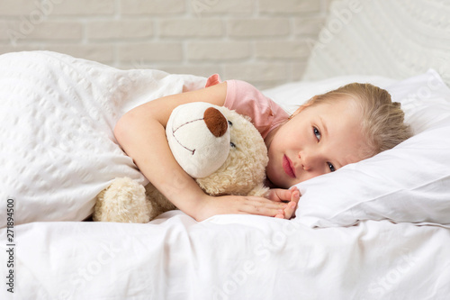 Cute little child girl sleeping with teddy bear in her bed