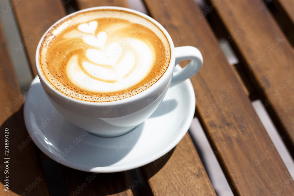 Hot cappuccino with froth and pattern on wooden background, top view