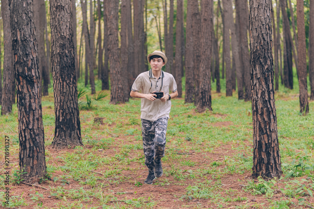 Asia man wears shirt, hat, and camouflage pants are running and taking photos at the forest.