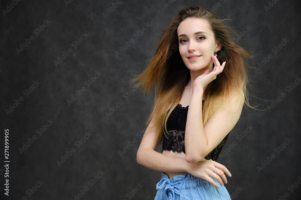 Fototapeta premium Photograph of a portrait of a beautiful girl woman with long dark flowing hair, happy life on a dark gray background. She is standing directly in front of the camera in various poses and smiling.