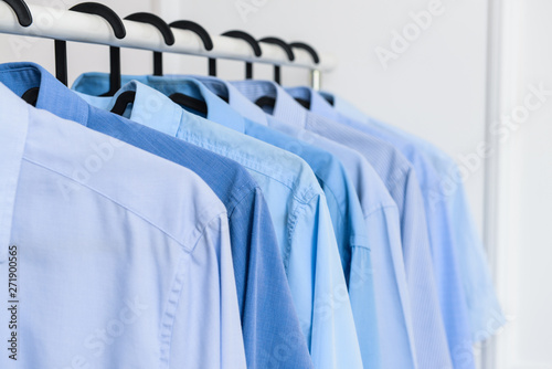 Rack with clothes after dry-cleaning near white wall, closeup