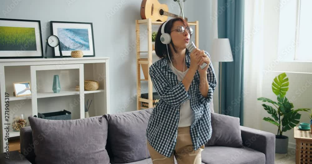 Happy young woman in headphones is singing in remote control dancing having fun in apartment. Joyful millennials, leisure time and funny activity concept.