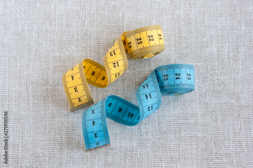 blue and yellow tailor measuring tape on a light gray linen background closeup