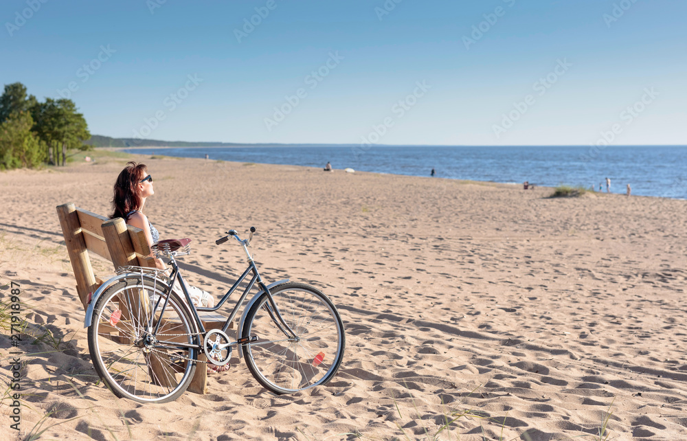 Middle-aged woman came on a Bicycle to the beach and resting sitting on a bench.