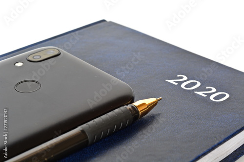 Closed notebook for new year with text 2020 on cover, ballpoint pen and black classic modern smartphone of rear side with fingerprint sensor and dual camera on white background. Isolated. Close up