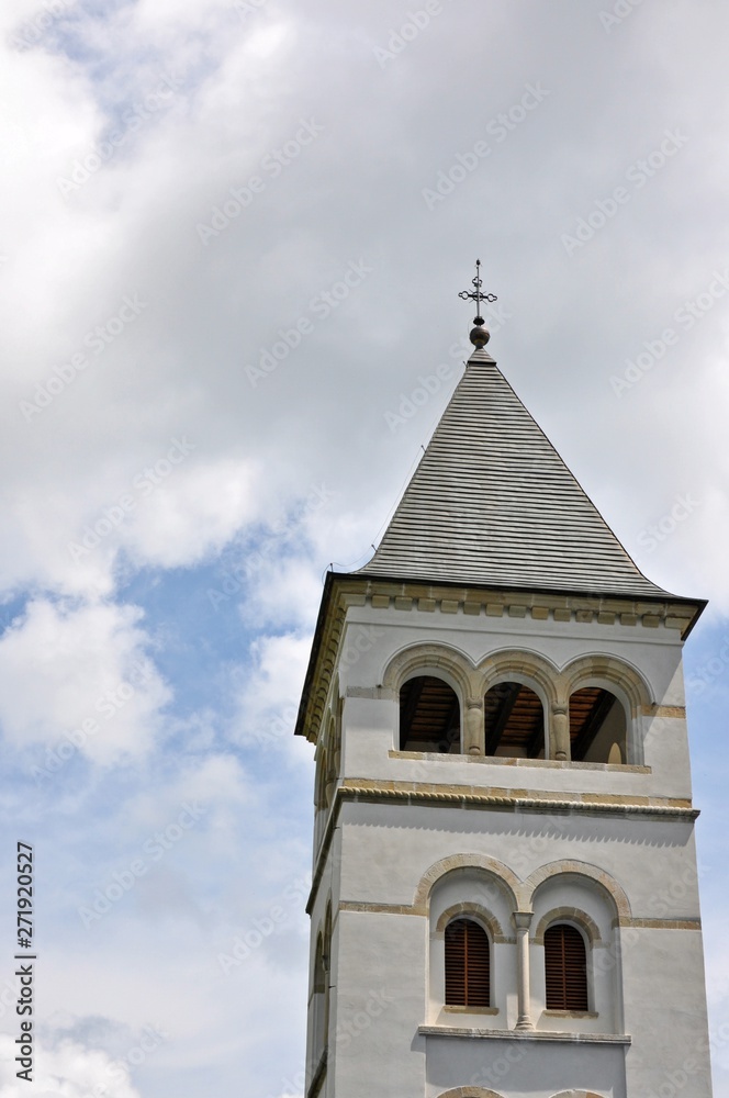 Fototapeta premium Bottom view of building turret with a cross on top on cloudy sky background.