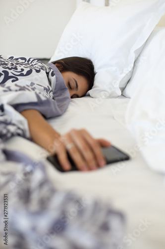 Young woman sleeping with her mobile phone in the hand. Smartphone addiction and sleep disorders concept.