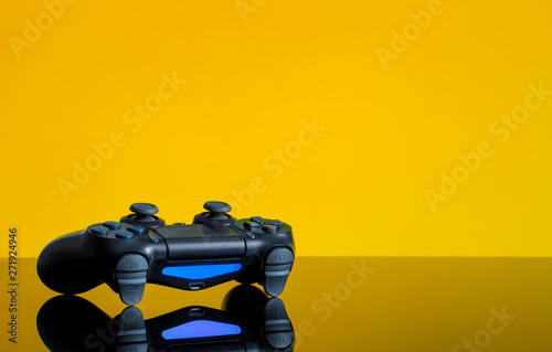 Modern black gamepad on a yellow back. Joystick black color on a smooth reflective table. Gaming concept photo