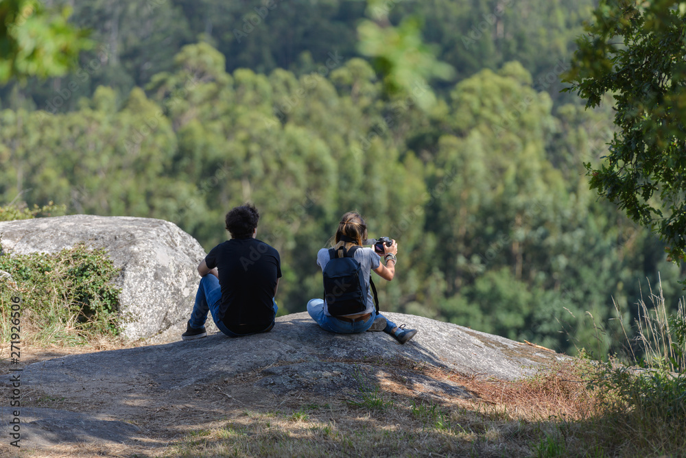 young couple taking photographs of the landscape with a reflex camera from the top of a cliff