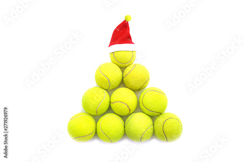 Santa hat on tennis ball on white snow background. Merry Christmas and New year concept with tennis balls. Yellow green color tennis balls in shape fir tree. Close up, sport lifestyle. Isolated. photo