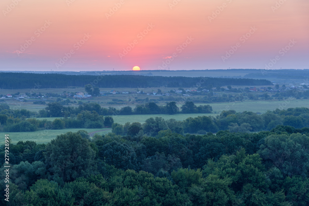 Sun rises in the early morning over the fields and forests