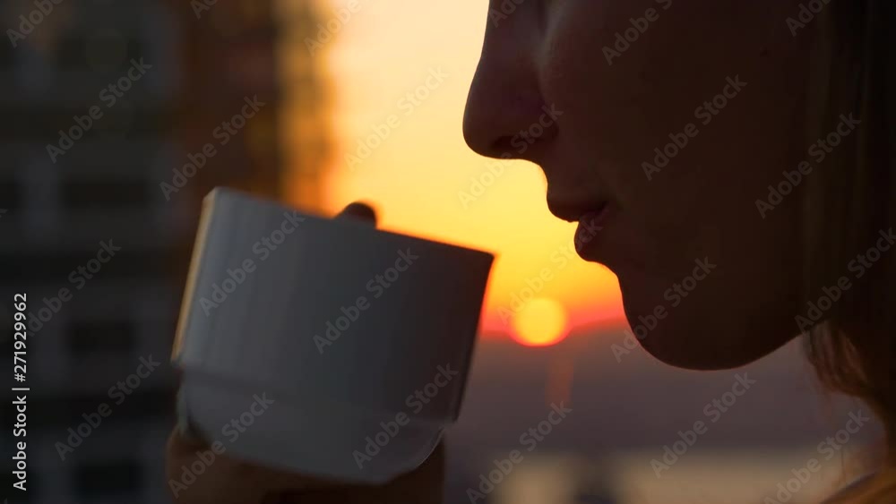 CLOSE UP, DOF: Unrecognizable woman takes a sip of healthy green tea while sitting in her hotel room at sunrise. Relaxed tourist girl drinking coffee and enjoying vacation on a beautiful sunny evening