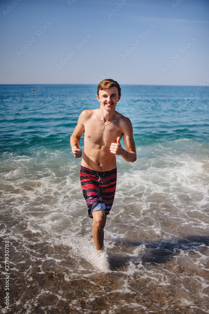 Beautiful young happy man Running along the waves in water at the sea beach. Turkey. Vacation. Sunlight. Place for text Close up. Summer vacation, honeymoon. Ocean sea Beautiful young happy man Running along the waves in water at the sea beach. Turkey. Vacation. Sunlight. Place for text Close up. Summer vacation, honeymoon. Ocean sea