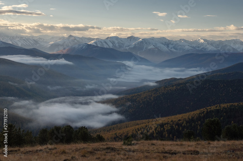 Dramatic sunset above the highland mountain valley in fog with ranges of snow peaks rocks