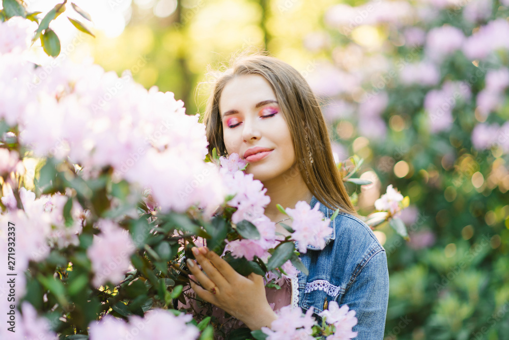 portrait of a beautiful girl with loose hair and makeup with her eyes closed near a Bush with pink rhododendron flowers in spring. The concept of peace, tranquility, happiness and enjoyment of nature