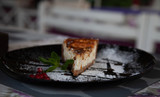 a slice of cottage cheese cheesecake on a large black plate decorated with mint and cranberries