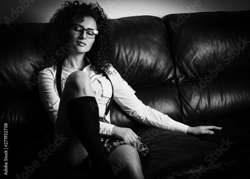 Sensual young sexy girl with curly hair dressed in student clothes: skirt and shirt , sitting on sofa. Black and White , Retro (vintage) style. -Picture.