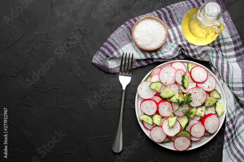 Fresh radish and cucumber salad and greens on a black concrete table. Salad of spring vegetables. ingredients for making salad. top view