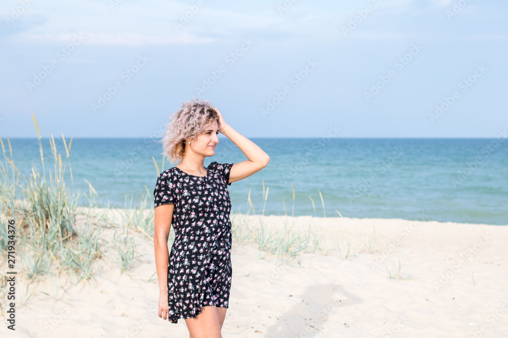 beautiful female with curly hairs in black dress in flowers is happy to be on the beach. Sea and grass on the background beautiful female with curly hairs in black dress in flowers is happy to be on the beach. Sea and grass on the background