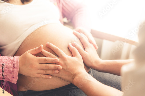 Pregnant couple of husband and wife feels love and relax at home. Young expecting woman holds baby in pregnant belly. Father take care of pregnant mother. Concept of maternity and pregnancy care. photo