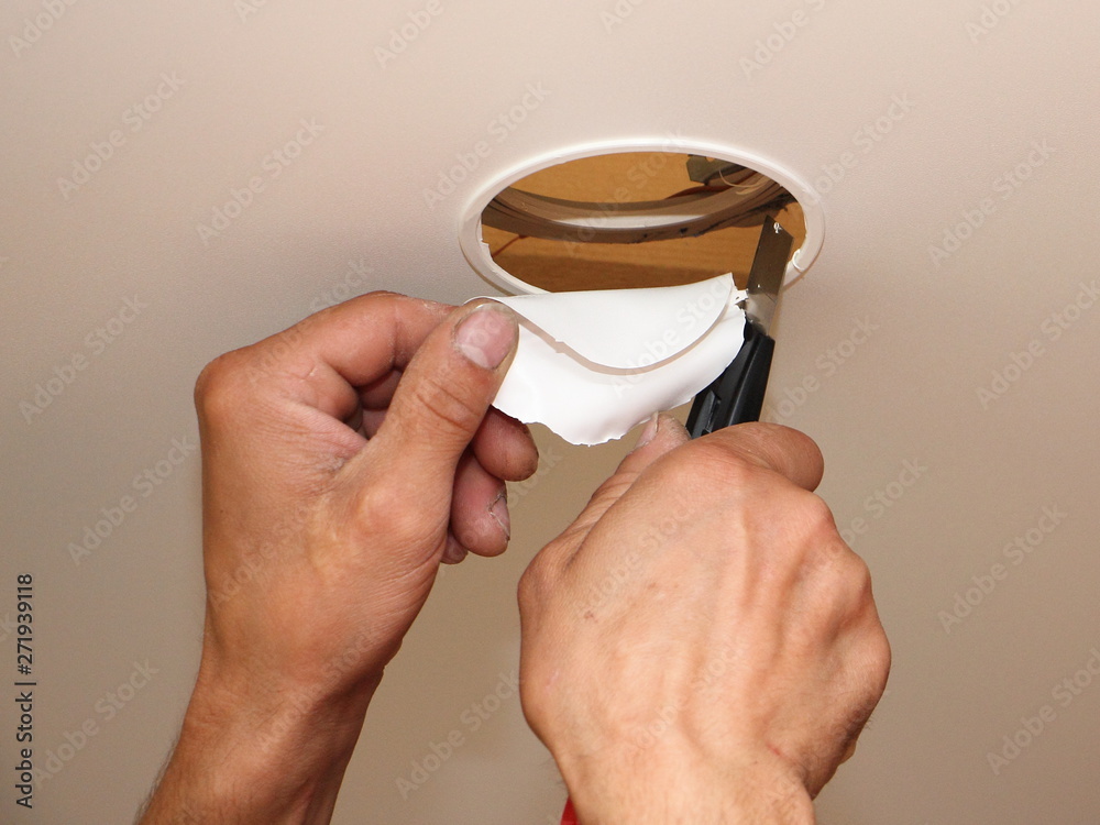 Men hands cutting a hole for the recessed spot light in the stretch
