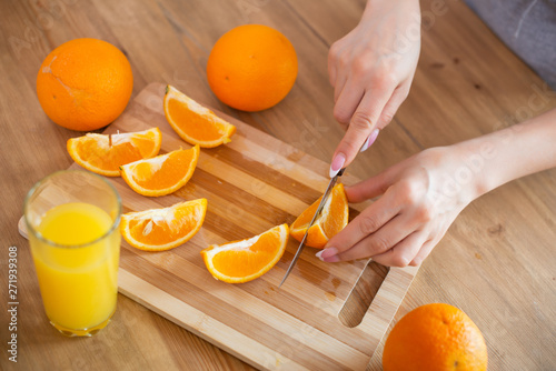 cooking, food and concept of veganism, vigor and healthy eating - close up of female hand cutting orange on slices