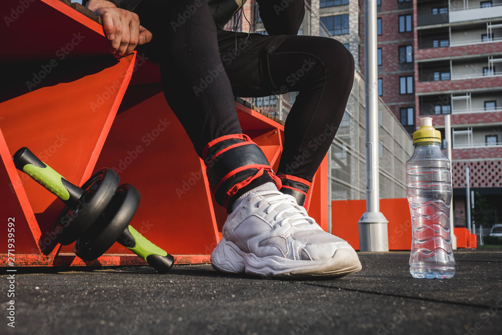 Fototapeta premium a man sits on an orange bench in black pants and white sneakers on the sports field.