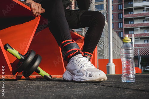 a man sits on an orange bench in black pants and white sneakers on the sports field.