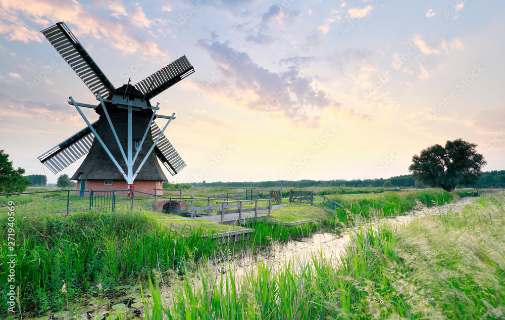 Dutch windmill by river at sunset