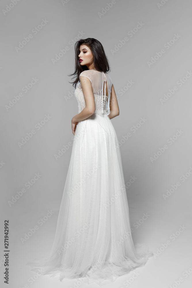 A side view of a gentle brunette model in classic white wedding dress, on white background.