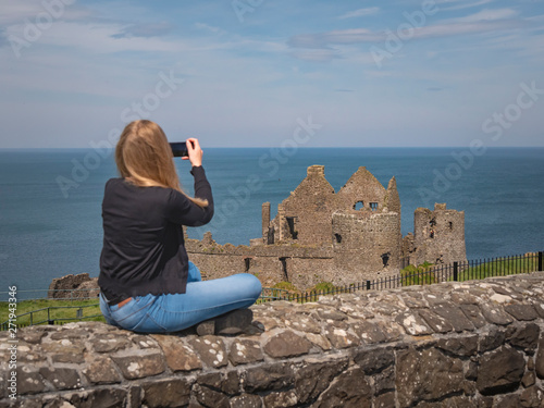 Young woman takes photos of Dunluce Castle in North Ireland - travel photography