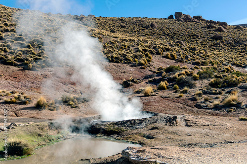 Atacama desert, Chile: Bright rising sun behind erupting Hot Geyser Of Steam in El Tatio Geysers field at early morning sunrise