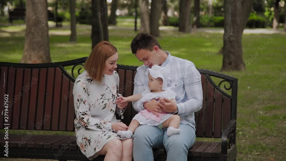 Happy young family with his son resting in the Park in the summer on a bench. A beautiful woman with her husband and a child sitting on a bench in the background of the urban landscape Happy young family with his son resting in the Park in the summer on a bench. A beautiful woman with her husband and a child sitting on a bench in the background of the urban landscape