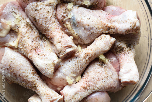 Raw chicken drumsticks are sprinkled with ground pepper, salt and garlic.