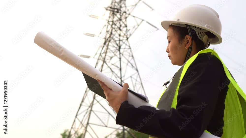 Asian senior electrical engineer working at site of big pole high voltage on sunset Asian senior electrical engineer working at site of big pole high voltage on sunset