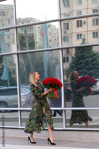 girl in a green dress with a bouquet of red roses at the mirror wall