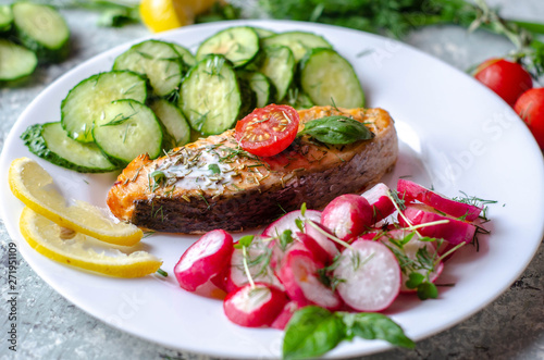 Salmon steak with lemon, tomatoes, cucumber and radish on a plate. Healthy seafood. Proper nutrition food.