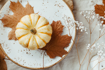 Top view on a decorated table setting for Thanksgiving dinner. Autumn ornate, white pumpkin on ceramic plates.