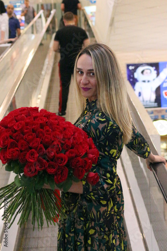 girl in green dress with a bouquet of red roses on the escalator