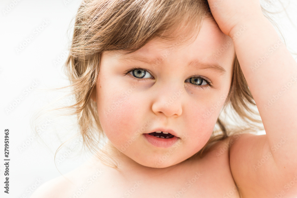 Baby girl close portrait isolated on neutral background. Beautiful child touching her hair and looking seriously 