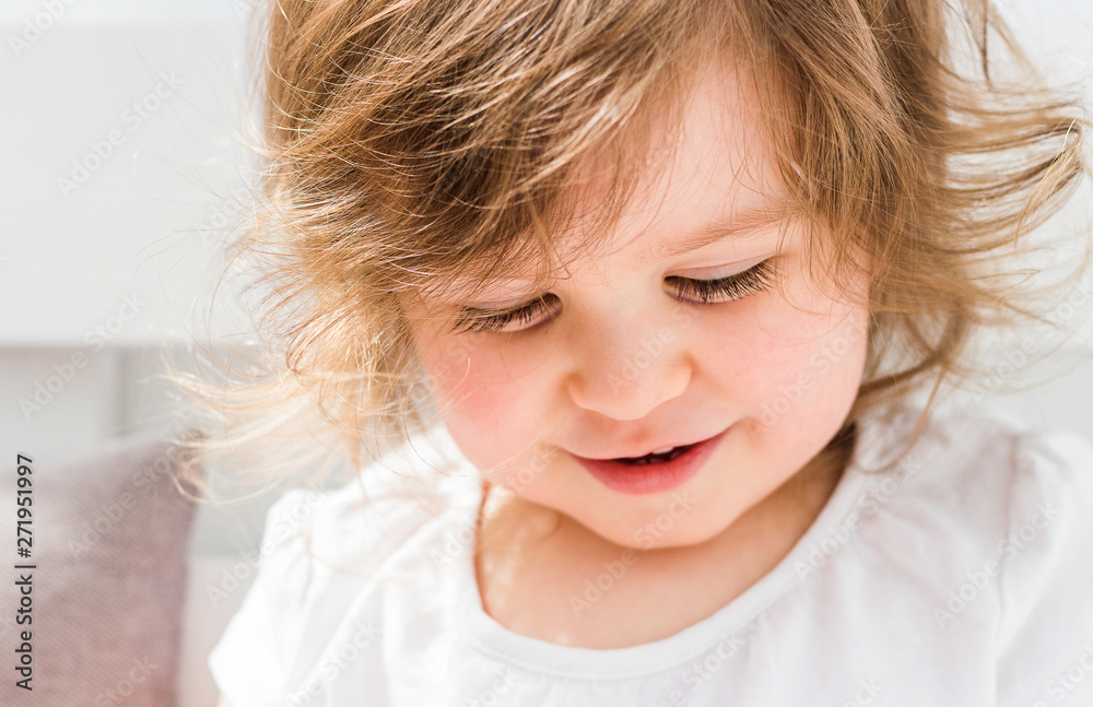 Beautiful smiling blonde baby girl looking down playing close portrait on light background Beautiful smiling blonde baby girl looking down playing close portrait on light background